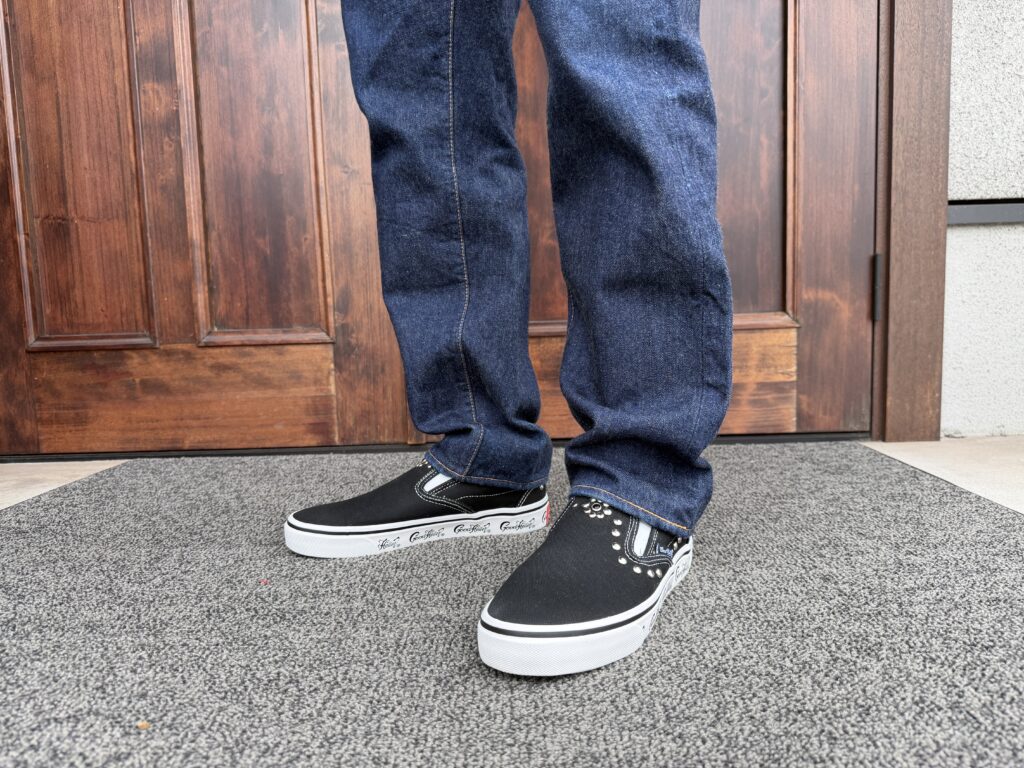 JELADOの濃紺デニムにGOOD HELLERの黒いスタッズスリッポンを合わせた男性の足元