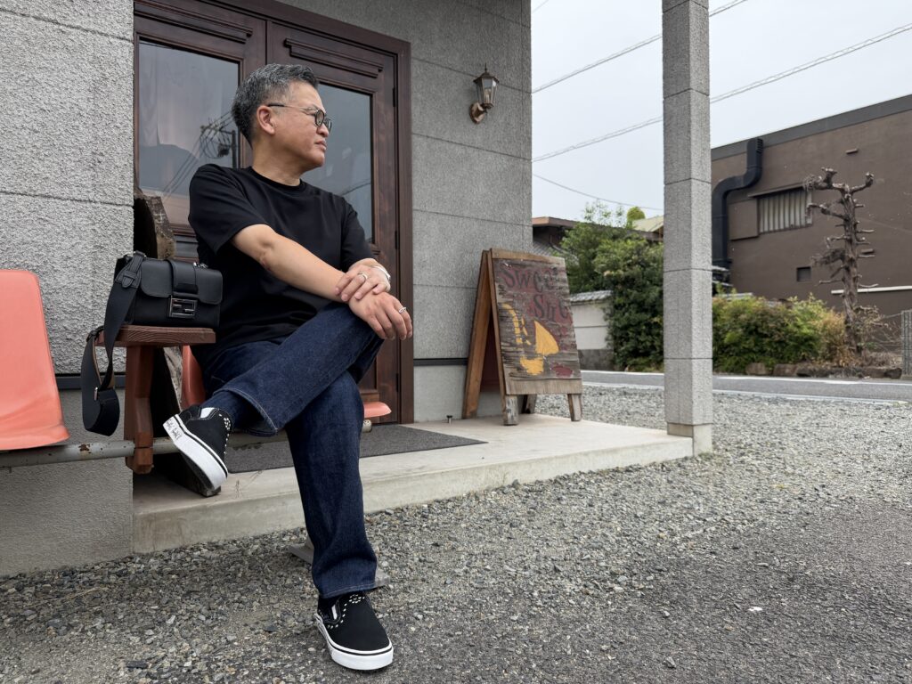 Brooks Brothersの黒TとJELADOの濃紺デニム、FENDIのバッグ、GOOD HELLERのスリッポンを合わせた50代男性のコーディネート